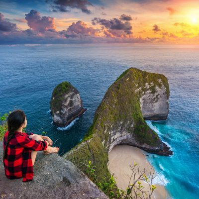 Woman sitting on cliff and looking at sunset at Kelingking Beach in Nusa penida island, Bali, Indonesia.